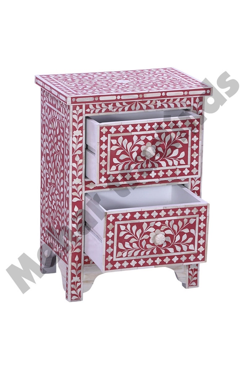 May include: A red wooden nightstand with two drawers. The drawers are decorated with white floral patterns and have bone inlay details. The nightstand has a floral design on the front and sides.