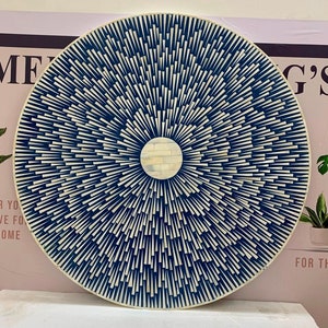 Könnte beinhalten: Ein rundes, weißes, dekoratives Tablett mit einem blauen und weißen geometrischen Muster. Das Muster besteht aus kleinen, dünnen, blauen Linien, die vom Zentrum des Tabletts ausstrahlen. Die Mitte des Tabletts ist ein weißer Kreis.