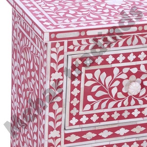 May include: A three-drawer chest with intricate floral bone inlay designs in white on a red background. The chest has a square top and rounded corners.