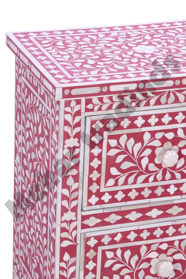 May include: A three-drawer chest with intricate floral bone inlay designs in white on a red background. The chest has a square top and rounded corners.