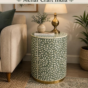 May include: A cylindrical side table featuring a sage green surface with an intricate white vine and leaf inlay pattern. The table has a solid gold-toned metal base and a smooth, flat top surface. The text Mehar Craft India is visible at the top.