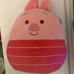 May include: Pink plush pig with a striped red and white body. The pig has a smiling face with brown eyes and a pink snout.