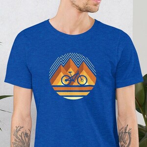 May include: A royal blue t-shirt with a retro-style graphic of a mountain bike in front of a sunset. The graphic is in shades of orange, yellow, and brown.