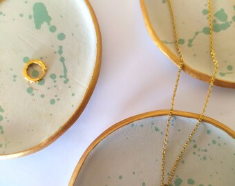 Puede incluir: Tres platos de cerámica con bordes dorados y un diseño de salpicaduras verdes. Los platos son perfectos para guardar joyas, anillos u otros objetos pequeños.