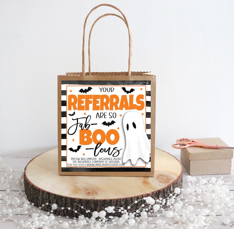 May include: A brown paper gift bag with a black and white striped design and a ghost graphic. The bag has a handle and says "Your Referrals Are So Fab-Boo-Lous".