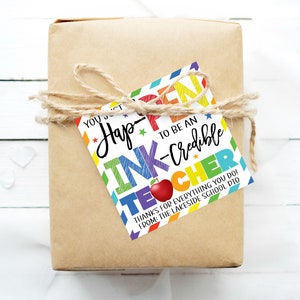 May include: A colourful gift tag with the text "You just happen to be an ink-credible teacher" and a red apple graphic. The tag is decorated with rainbow stripes and stars. The text "Thanks for everything you do! From: The Lakeside School PTO" is printed at the bottom.