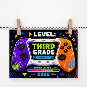 Può includere: Una stampa colorata con un design di controller per videogiochi. Il controller è diviso in sezioni viola e arancioni, con la scritta "THIRD GRADE COMPLETE" al centro. Viene visualizzato anche l'anno "2026".