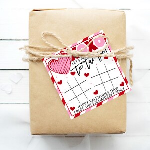 May include: A brown gift box wrapped with twine and a red and white Valentine's Day tic-tac-toe game card. The card says "Let's Play Tic Tac Toe! Happy Valentine's Day! From the Williamson Family."