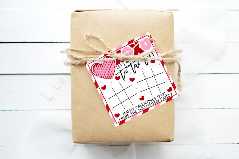May include: A brown gift box wrapped with twine and a red and white Valentine's Day tic-tac-toe game card. The card says "Let's Play Tic Tac Toe! Happy Valentine's Day! From the Williamson Family."