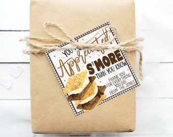 Może przedstawiać: Brązowe pudełko prezentowe z etykietą z napisem "You're Appreciated S'more Than You Know" z grafiką s'more. Etykieta ma brązowo-białą kratkę i brązowe kropki.