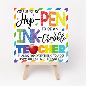 May include: A colourful sign with the text "You just so Hap-PEN to be an INK-Credible TEACHER" with a red apple and stars. The sign is on a small wooden easel. The text "THANKS FOR EVERYTHING YOU DO! FROM: THE LAKESIDE SCHOOL PTO" is at the bottom of the sign.