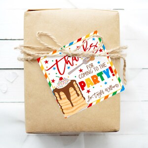 May include: A wrapped gift in brown paper tied with twine, featuring a colorful tag. The tag reads "Thanks for coming to the party!" with a pancake illustration and the name "Taylor Williams."