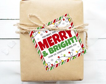 May include: A white gift tag with red and green striped borders and a string of colorful lights. The tag reads "You make this Merry & Bright! From: The Sunnyside School PTO".