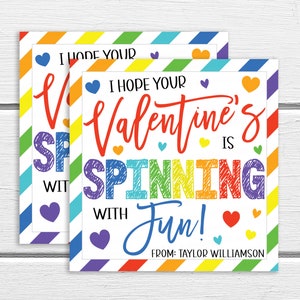 May include: Two colorful Valentine's Day cards with a rainbow striped background. The text on the card reads "I hope your Valentine's is spinning with fun!" with a signature at the bottom that reads "From: Taylor Williamson".