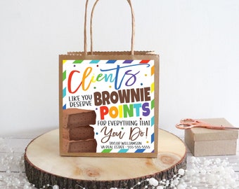Puede incluir: Una bolsa de papel marrón con un diseño de rayas de colores y una etiqueta que dice "Los clientes como tú se merecen puntos brownie por todo lo que hacen!" con una pila de brownies y una tarjeta de visita con información de contacto.