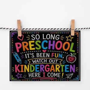 Könnte beinhalten: Ein schwarzes Schild im Tafelstil mit farbenfrohem Text und Illustrationen, darunter ein Herz, ein Stern, ein Apfel und ein Bleistift. Auf dem Schild steht "So Long Preschool, It's Been Fun, Watch Out Kindergarten, Here I Come!" Es wird von zwei Holzklammern gehalten.