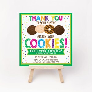 May include: A colorful sign on a small wooden easel. The sign says "THANK YOU - FOR YOUR SUPPORT! - ENJOY YOUR COOKIES!" and features images of cookies. Contact information is at the bottom.