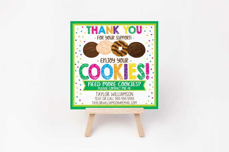 May include: A colorful sign on a small wooden easel. The sign says "THANK YOU - FOR YOUR SUPPORT! - ENJOY YOUR COOKIES!" and features images of cookies. Contact information is at the bottom.