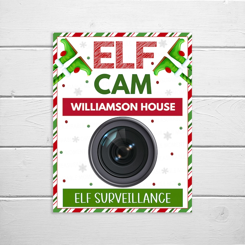 May include: A white sign with red and green stripes. The sign says "Elf Cam" with a camera lens graphic and the text "Williamson House" and "Elf Surveillance".