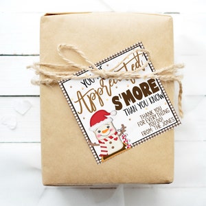Puede incluir: Una caja de regalo marr&oacute;n con una etiqueta de regalo blanca y marr&oacute;n atada con cuerda. La etiqueta de regalo presenta una ilustraci&oacute;n de un mu&ntilde;eco de nieve y el texto "You're Appreciated S'more Than You Know. Thank You For Everything You Do! From: The Jones."