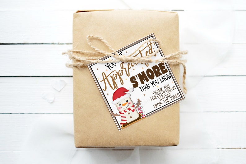 Puede incluir: Una caja de regalo marr&oacute;n con una etiqueta de regalo blanca y marr&oacute;n atada con cuerda. La etiqueta de regalo presenta una ilustraci&oacute;n de un mu&ntilde;eco de nieve y el texto "You're Appreciated S'more Than You Know. Thank You For Everything You Do! From: The Jones."
