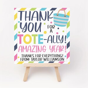 May include: A colourful thank you card with a striped tote bag design. The card says "Thank You for a Tote-ally Amazing Year! Thanks for everything! From: Taylor Williamson."