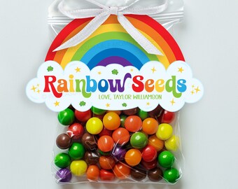 Op de afbeelding: Een doorzichtige plastic zak gevuld met kleurrijke snoepjes, vastgebonden met een wit lint en een regenboogvormig label met de tekst "Rainbow Seeds" en de naam "Love, Taylor Williamson" eronder.