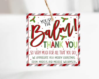 Pode incluir: Uma etiqueta de presente de Natal listrada em vermelho e branco com um design de azevinho verde. A etiqueta diz "You're the Balm! Thank You" e "So very much for all that you do! We appreciate you! Merry Christmas. From: Marcus and Michelle Williamson."