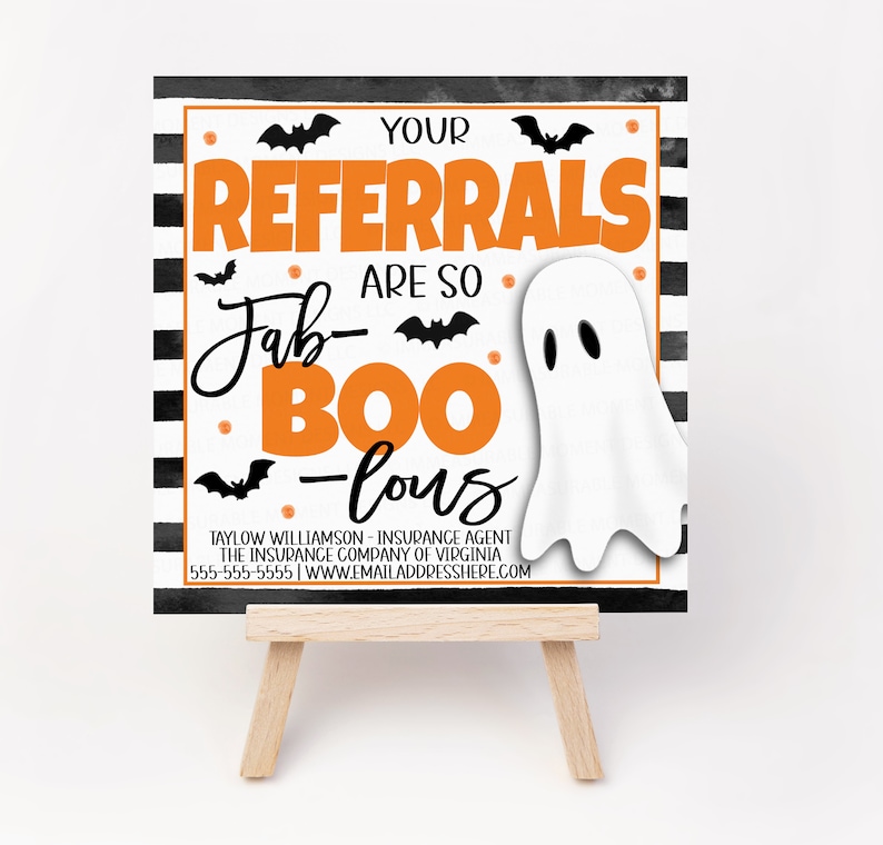 May include: A black and white striped sign with orange text that reads "Your Referrals Are So Fab-Boo-Lous". A white ghost with black eyes is on the sign. The sign is on a small wooden easel.