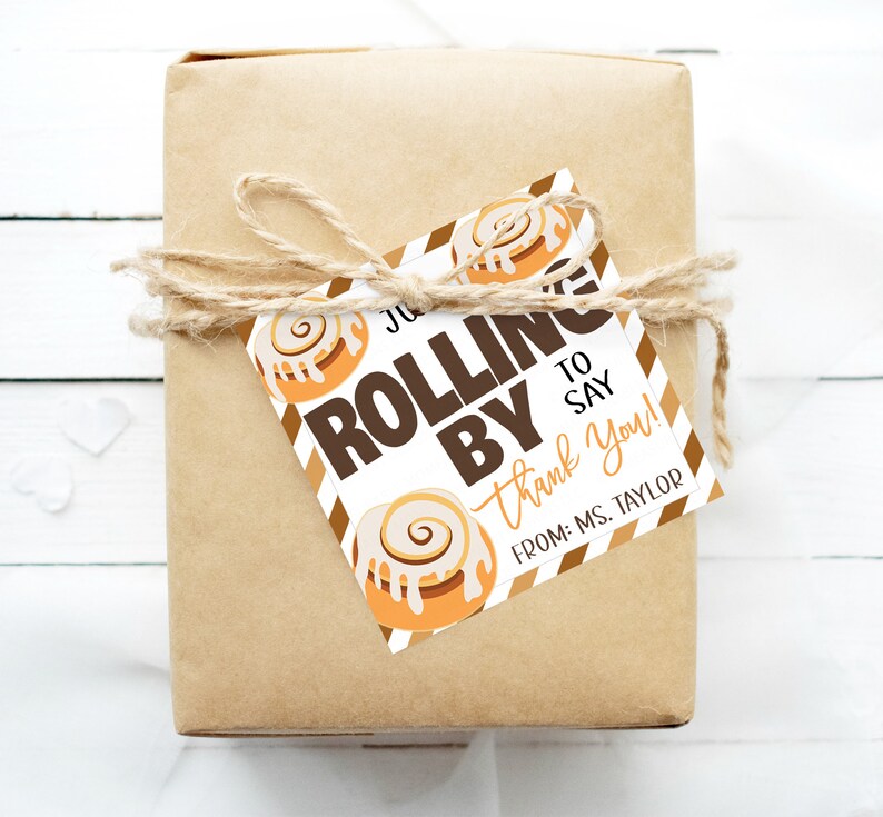 Może przedstawiać: Biała etykieta prezentowa w brązowe i pomarańczowe paski. Etykieta zawiera ilustrację cynamonowego rogalika i tekst "Just rolling by to say thank you! From: Ms. Taylor".