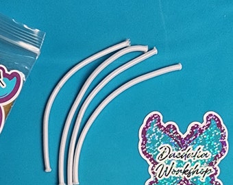 May include: Five white elastic bands, approximately 6 inches long, are arranged in a curved shape on a blue background. The elastic bands are commonly used for crafts, hair ties, or other DIY projects.
