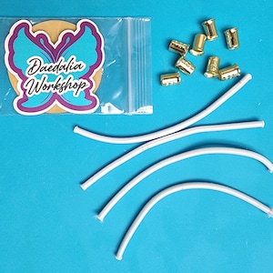 May include: A set of white elastic cord and gold metal cord ends. The cord ends are in a small plastic bag with a butterfly logo that says "Daedalia Workshop".