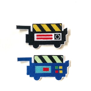 May include: Two embroidered patches in the shape of a pixelated cart. One is black with a yellow and black striped top, red stripes, and a white circle. The other is blue with a green and black striped top, and red and yellow squares.