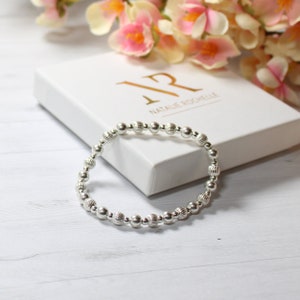 Può includere: Un braccialetto in argento con perline dal design testurizzato. Il braccialetto è su una scatola bianca con la scritta "Natalie Rochelle" stampata su di essa.