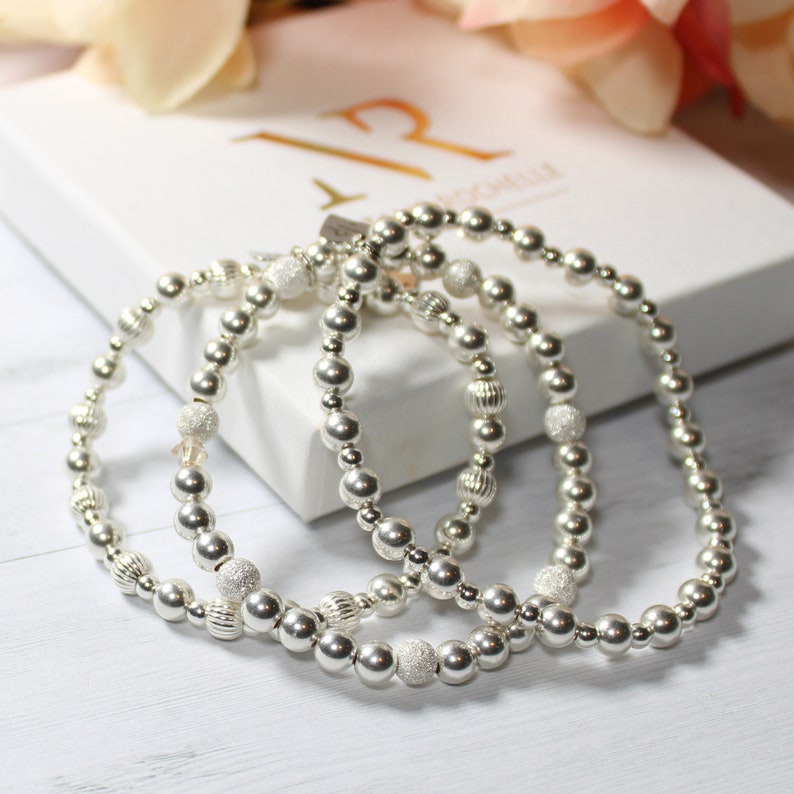 May include: Three silver beaded bracelets with a sparkly finish. The bracelets are stacked on top of each other.