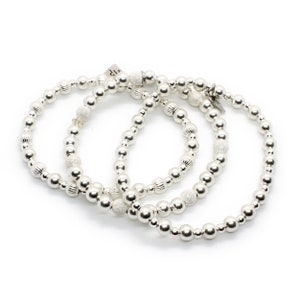 May include: Three silver beaded bracelets with different textures. The bracelets are stacked on top of each other.