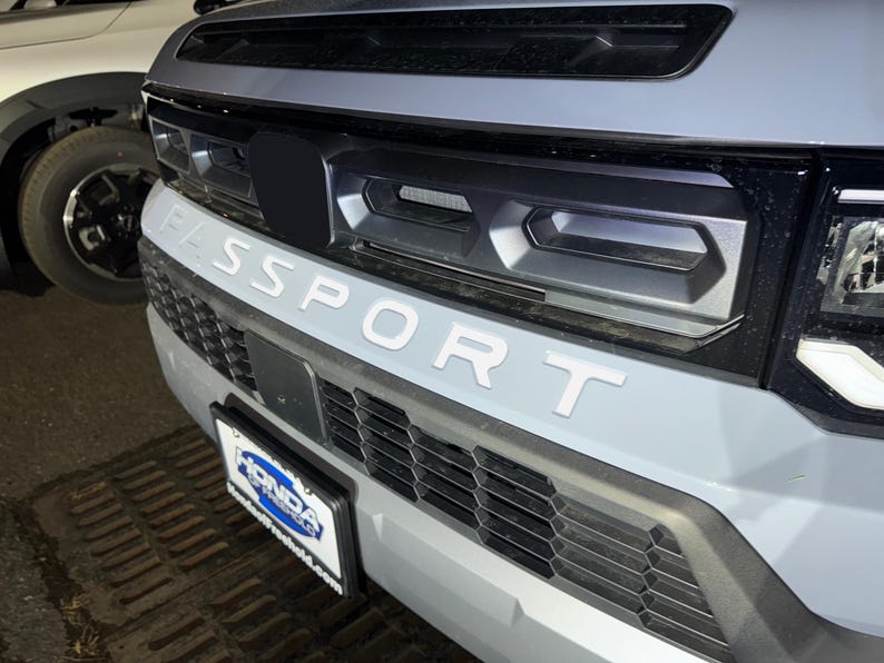 May include: A gray SUV with a black grille and the word "SPORT" in white letters on the front bumper.