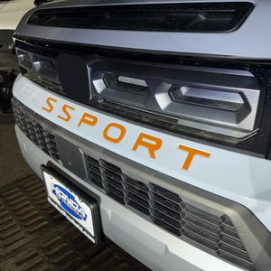 May include: A gray car with a black grille and the word "SPORT" in orange letters on the front bumper.