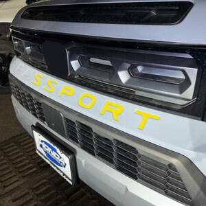 May include: A gray car with a black grille and the word "SPORT" in yellow letters on the front bumper.
