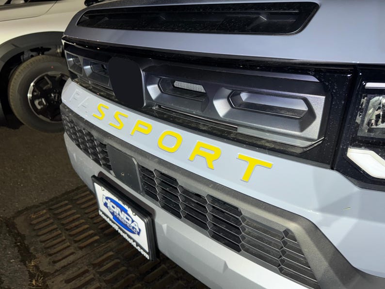May include: A gray car with a black grille and the word "SPORT" in yellow letters on the front bumper.