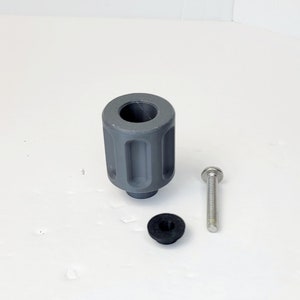 Puede incluir: Un pomo de plástico gris con una superficie texturizada, un tornillo plateado y una arandela de goma negra.