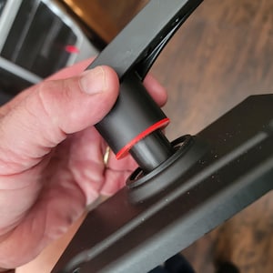 Puede incluir: Componente metálico negro con un anillo rojo. El componente parece ser parte de una estructura más grande, posiblemente un mueble o equipo. El diseño es moderno y funcional, con un enfoque en líneas limpias y una estética minimalista.