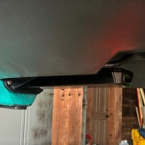 May include: A black metal bracket attached to the underside of a teal colored vehicle. The bracket is mounted to a wooden surface.
