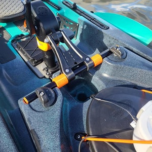 Puede incluir: Un soporte de motor de kayak negro y naranja con un asiento de kayak negro y gris en el fondo.