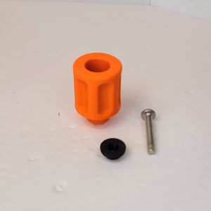 Puede incluir: Una pieza de plástico naranja impresa en 3D con un tornillo y una arandela de plástico negro. La pieza tiene una forma cilíndrica con un agujero en el centro y una serie de crestas alrededor del exterior.