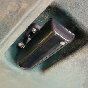 May include: A black plastic storage box with a mounting bracket. The box is attached to a gray surface with screws.