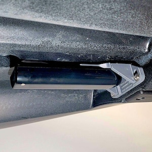 Può includere: Una maniglia cilindrica nera montata su una superficie grigio scuro con una staffa metallica angolare grigio chiaro. La staffa presenta una piccola vite argentata e un testo in rilievo che riporta Garmin e Panoptix, fissando la maniglia.