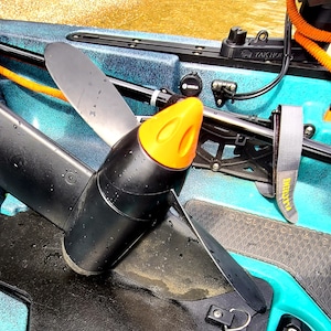 May include: A black electric motor with an orange propeller guard mounted on a turquoise kayak. The motor has a black propeller blade and a black and gray power cord.