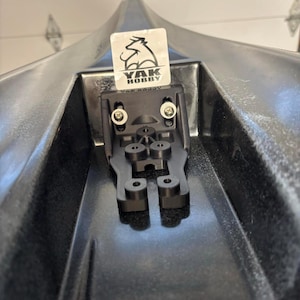 May include: Black kayak with a black mounting bracket. The bracket is secured with two silver screws and features a YAK HOBBY sticker. The kayak's interior is visible, showing its shape and design.