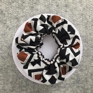 May include: A black, white, and brown patterned scrunchie with a geometric design.